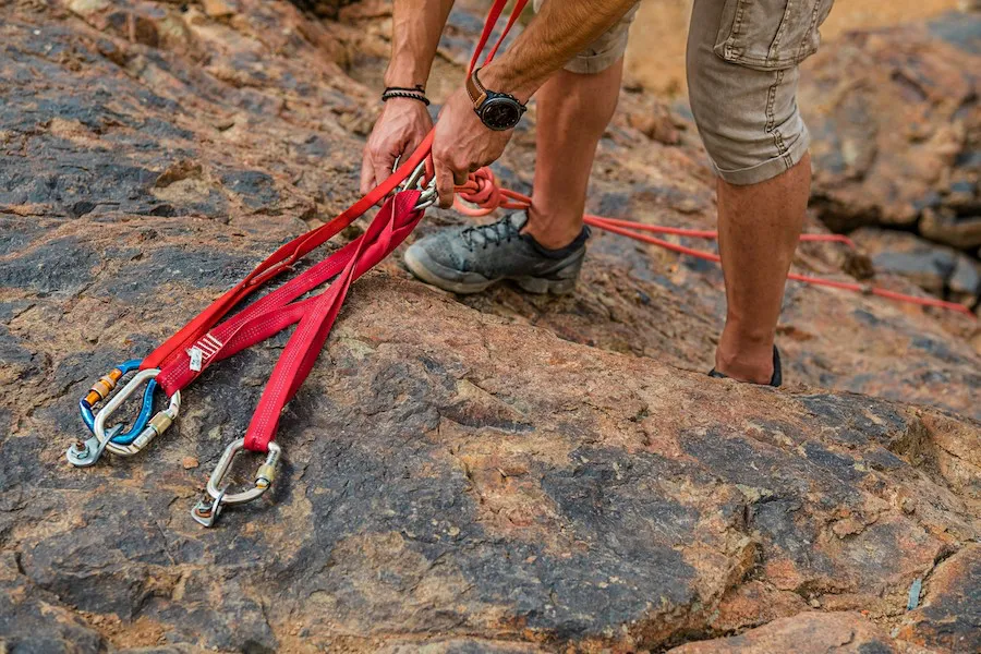 A climber's hands preparing red ropes and carabiners on a rock face