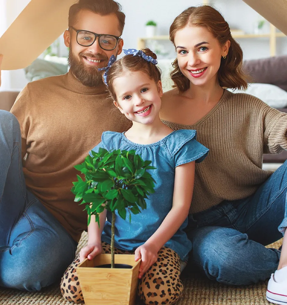 A smiling family sitting together holding a small potted plant