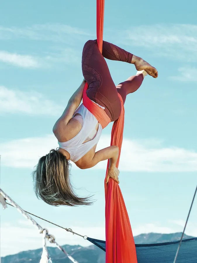 A woman hanging upside down on red aerial silks against a blue sky